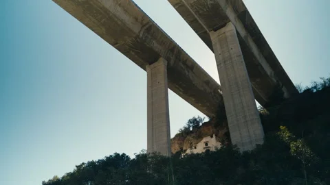 Massive concrete bridge over canyon with small house beneath 動画素材 333797347