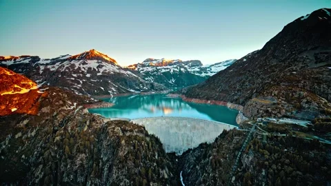 Massive concrete dam holding back turquoise mountain lake at sunrise cinematic Stock Footage 344241535