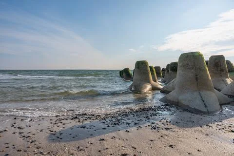 Massive concrete wave breakers stand by the sea, covered with green algae. Stock Photos
