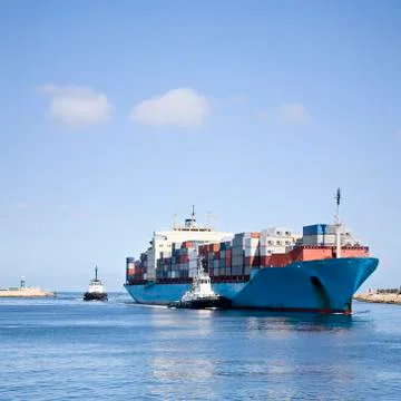 Massive container ship entering river mouth assisted by two tugs Stock Photos