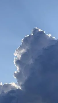 Massive cumulus cloud edge illuminated by bright sunlight against a clear blue Stock Photos