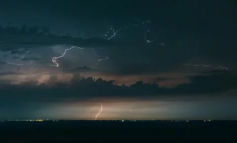 Massive drammatic cloud to ground lightning bolts hitting the horizon of city Stock Photos