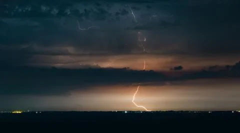 Massive drammatic cloud to ground lightning bolts hitting the horizon of city Stock Photos
