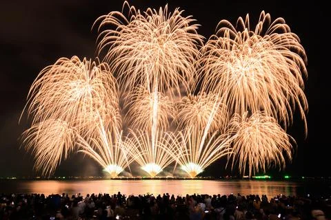 Massive Golden Fireworks Exploding Over Ocean With Crowd On Beach At Night .. Stock Photos