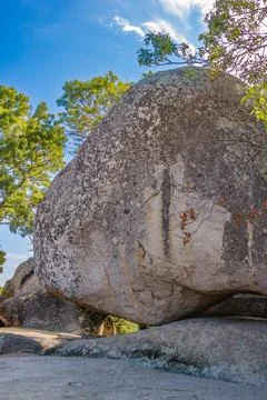 Massive granite boulder balanced on smaller rocks with forest trees and blu.. Stock Photos