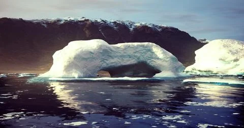 Massive ice arch floats in calm waters near rugged mountains at dawn Stock Illustration