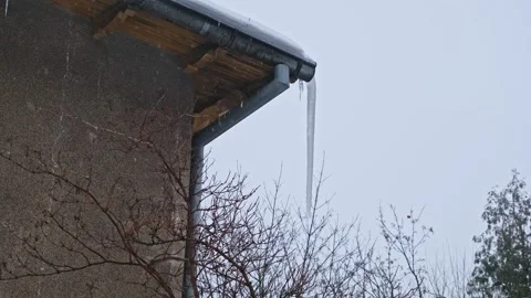 Massive Long Dangerous Icicle Hanging from Frozen Rain Gutter Posing Hazard Stock Footage 331857631