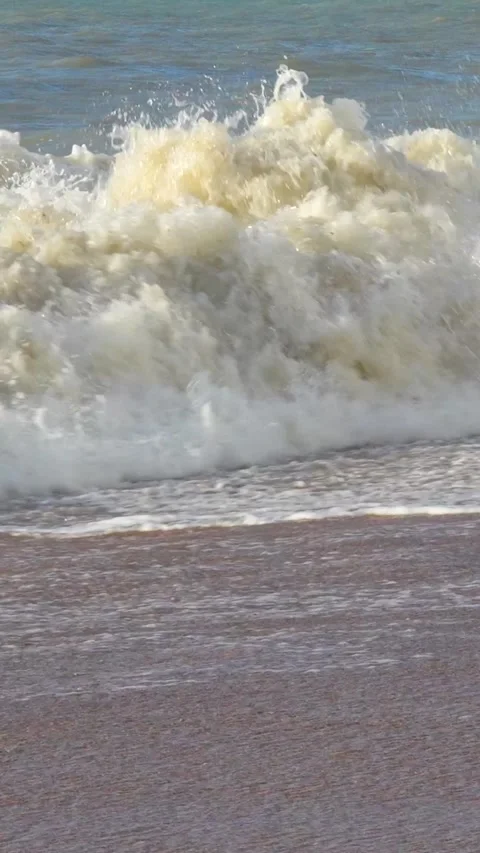 Massive ocean wave crashing onto sandy shore displaying powerful marine dynamics 库存影片 308877466