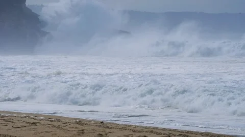 Massive Ocean Waves Crashing onto Sandy Shoreline with Misty Cliffs in the Stock Footage 297511313