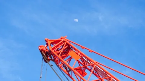 Massive red crane with afternoon moon and gently moving clouds in a blue sky Stock Footage 194214224