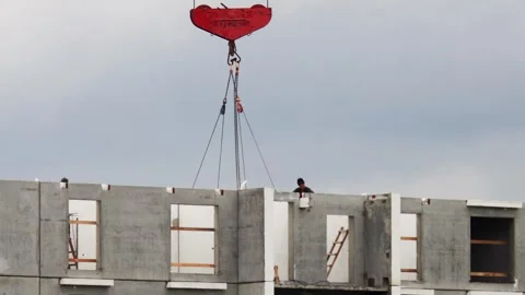 Massive red crane hook. Heavy concrete wall panels. Construction worker guides Stock Footage 323912354