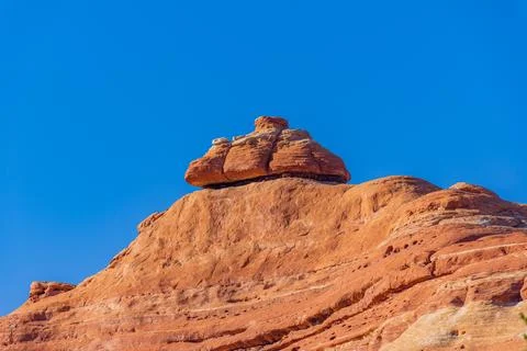 A massive red rock cap rests on a sloping cliff against a clear blue sky. Stock Photos