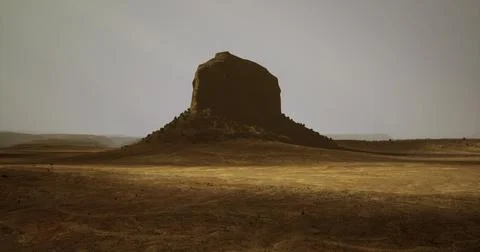 Massive rock formation rises from barren landscape under muted sky Stock Illustration