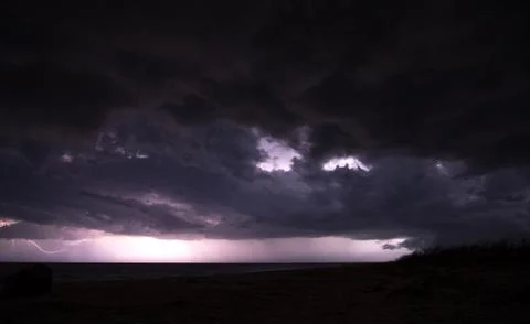 Massive thunderstorm with black cloud over the sea and lightings on the horizon 库存照片