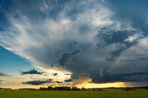 Massive thunderstorm cloud rising above a rural landscape during sunset Stock Photos