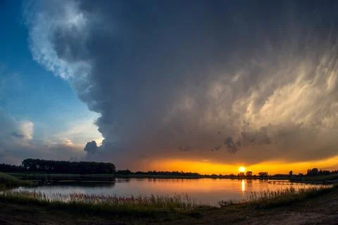Massive Wall of Dark Storm Clouds Above Lake at Bright Sunset Stock Photos