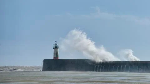Massive waves crash over harbour wall onto lighthouse during huge storm on En Foto stock