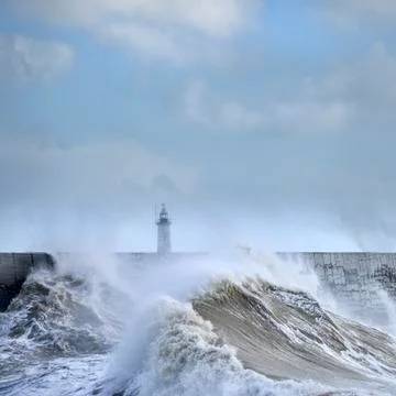 Massive waves crash over harbour wall onto lighthouse during huge storm on En Stock Photos