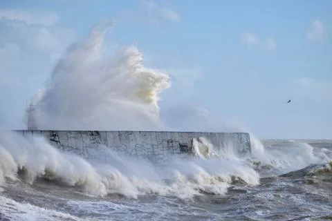 Massive waves crash over harbour wall onto lighthouse during huge storm on En 스톡 사진