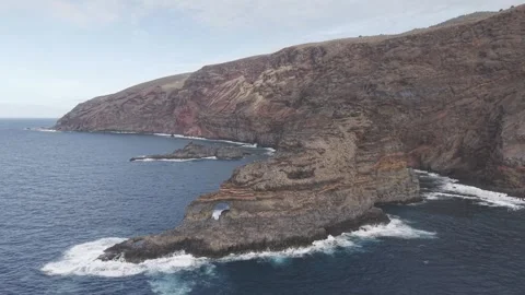 Massive waves smashing rocky cliffs in La Palma, exposing dramatic stone arch Stock Footage 308404859