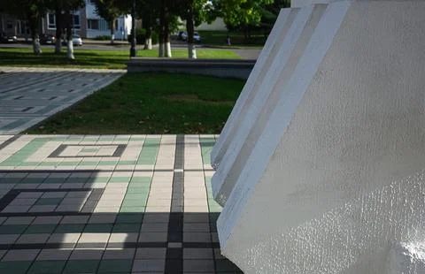 Massive white concrete structural element stands next to patterned green and Stock Photos