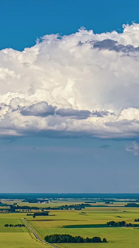 Massive white cumulonimbus cloud bubbling up over green agricultural fields and Stock Footage 337155995
