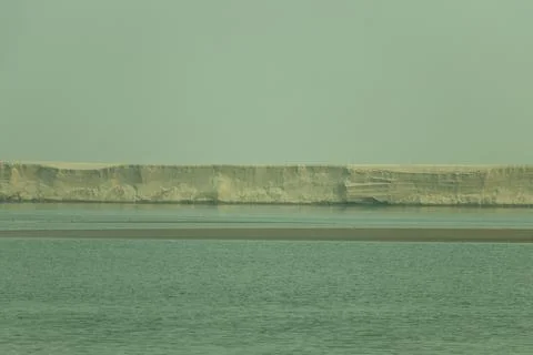 A massive white sandy cliff rises over a calm riverscape Stock Photos
