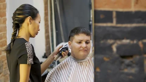 The master adjusts the speed of the tool for shaving the black hair of a woman Stock Footage 258050866