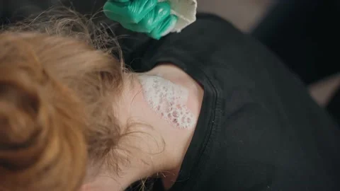 Master applied healing foam in skin and wipe neck client after tattoo session Stock Footage 219549356