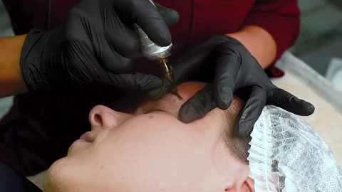 The master applies eyebrow makeup paint to the client with a typewriter. Stock Footage 131980311
