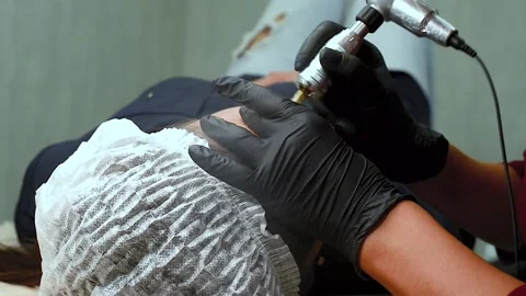 The master applies eyebrow makeup paint to the client with a typewriter. Stock Footage 131980321