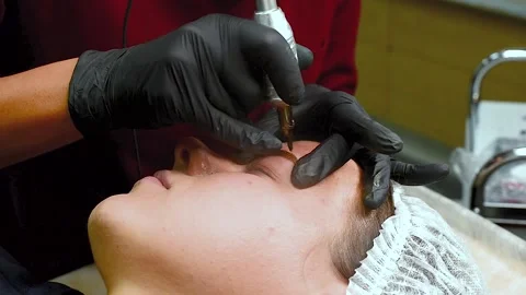 The master applies eyebrow makeup paint to the client with a typewriter. Stock Footage 131980653
