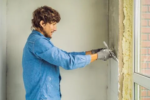 Master is applying white putty on a wall and smearing by putty knife in a room Stock Photos