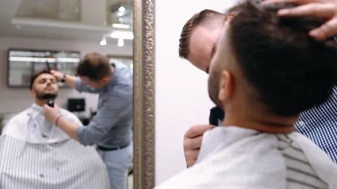 A master barber shortens and arranges a client's beard in a beauty salon or Stock Footage 144452712