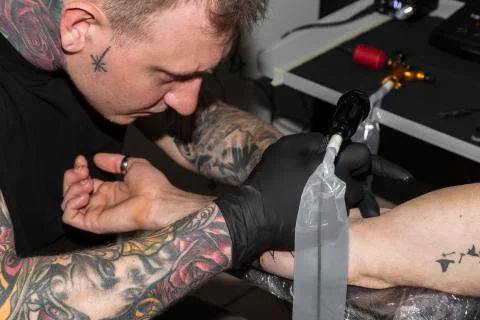 Master bends over man's arm and makes tattoo on it Stock Photos