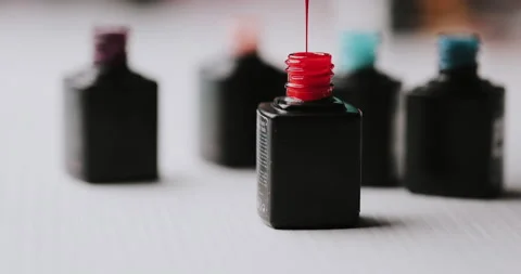 Master in black gloves holds red nail polish with an open bottle and a drop drip Stock Footage 149367777