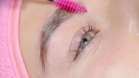 Master is brushing hair of eyebrows of young female client in beauty studio 스톡 동영상 96998587