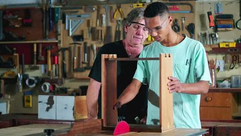 Master carpenter guiding apprentice at carpentry workshop, boss teaching st.. Stock Photos