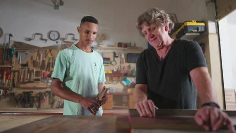 Master Carpenter Guiding Apprentice on Wood Sawing in Workshop, Young Appre.. Foto stock