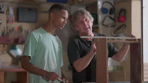 Master carpenter teaching apprentice the process of furniture building and .. Stock Footage 247307633