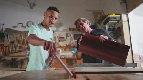 Master Carpenter working at carpentry workshop with his young apprentice, s.. Stock Photos