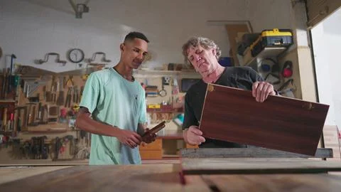 Master Carpenter working at carpentry workshop with his young apprentice, s.. Foto stock
