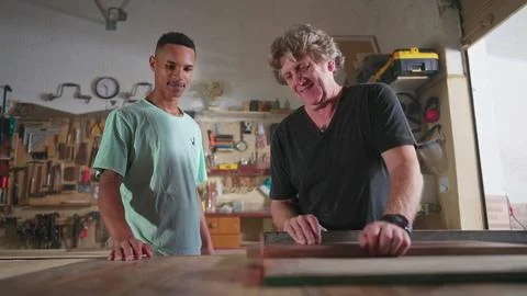 Master Carpenter working at carpentry workshop with his young apprentice, s.. Stock Photos
