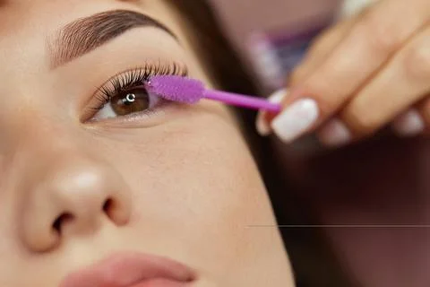 Master combs eyelashes of client after eyelash extension procedure Stock Photos