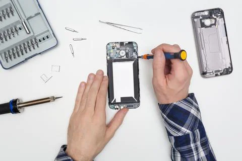 Master disassembles a broken mobile phone with a screwdriver. Man repairs a Stock Photos