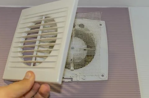 The master disassembles a wall-mounted household fan in the bathroom for service Stock Photos