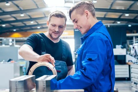 Master discussing a workpiece with his apprentice or trainee Stock Photos