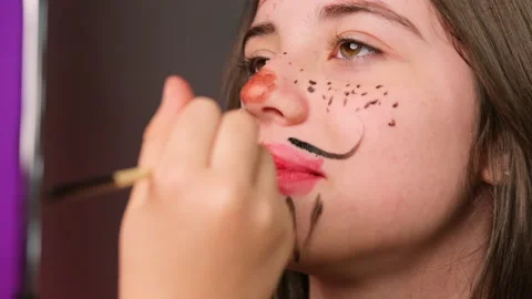 Master draws an aquagrim pattern on a child's face in the studio preparing her Video stock 162763649