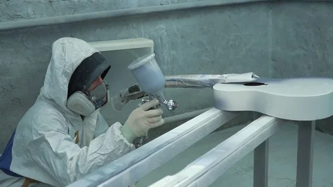 Master is engaged in applying a gray coat of paint on a white guitar using a Vídeo Stock 74021807