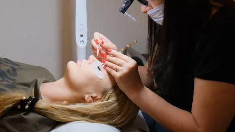 Master enlarges large eyelashes for a client in a beauty salon. eyelash Stock Photos
